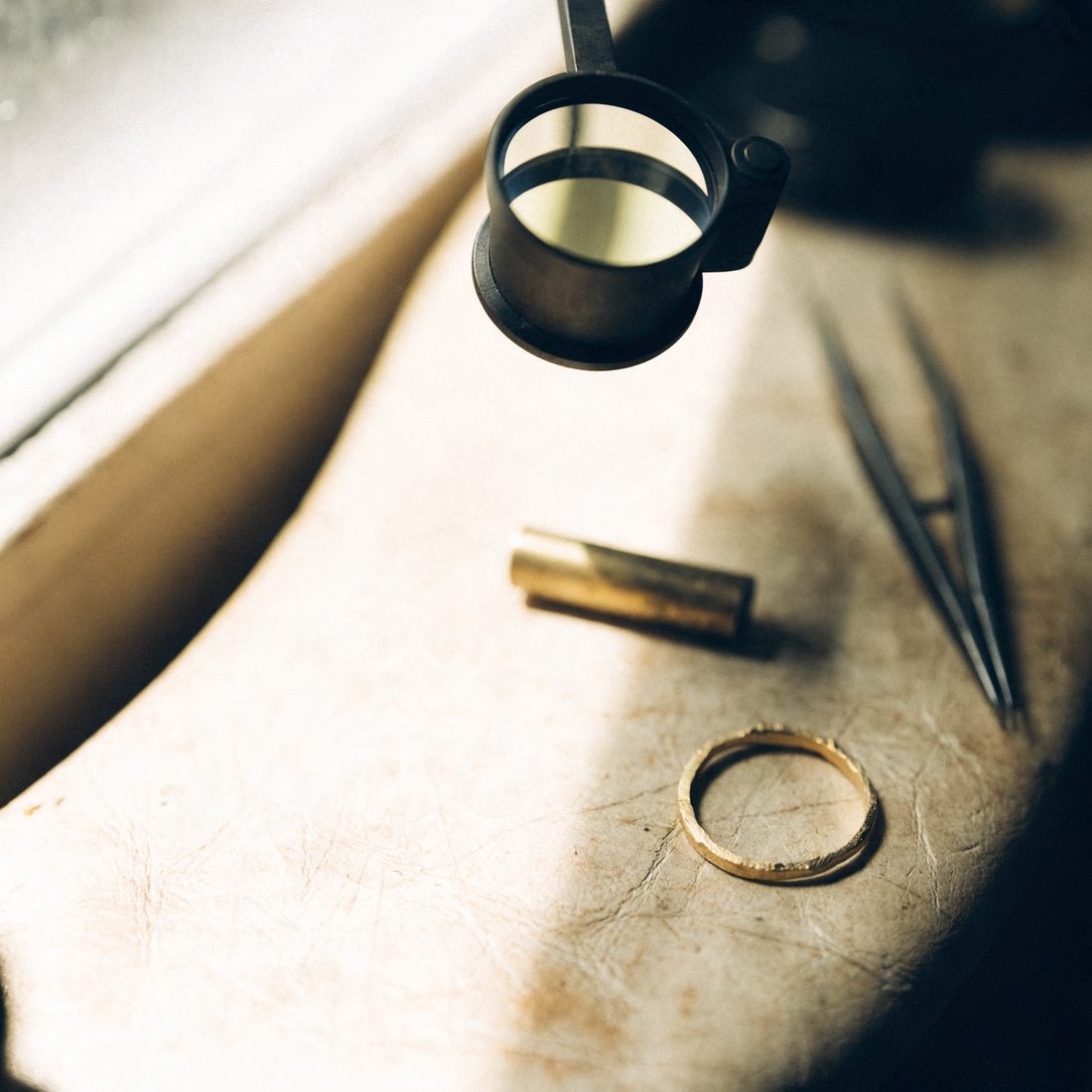 A jeweller's loupe, tweezers and an unfinished gold ring on a workbench