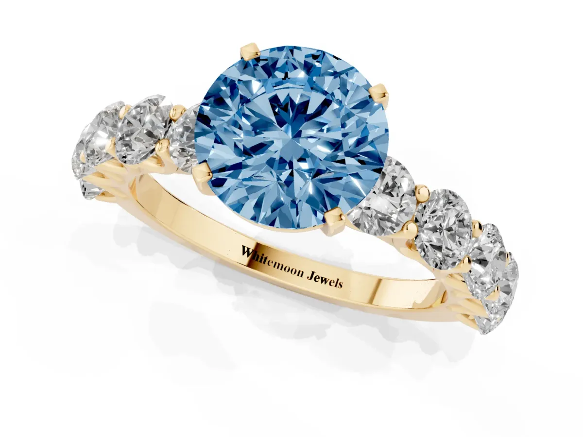 Fancy Blue Round Cut Diamond Prong Setting with Side Stones on a Pave Band Yellow gold