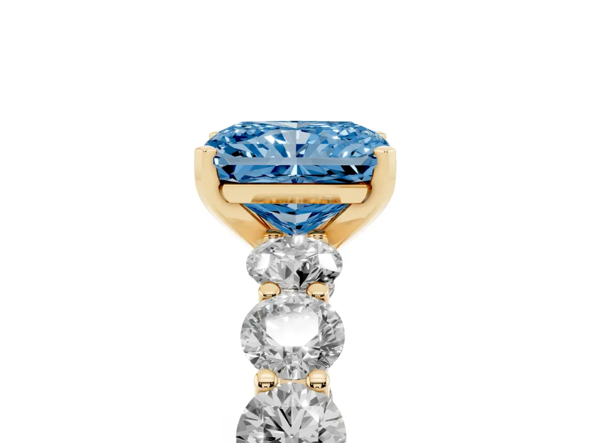 Fancy Blue Radiant Cut Diamond Prong Setting with Side Stones on a Pave Band Yellow gold