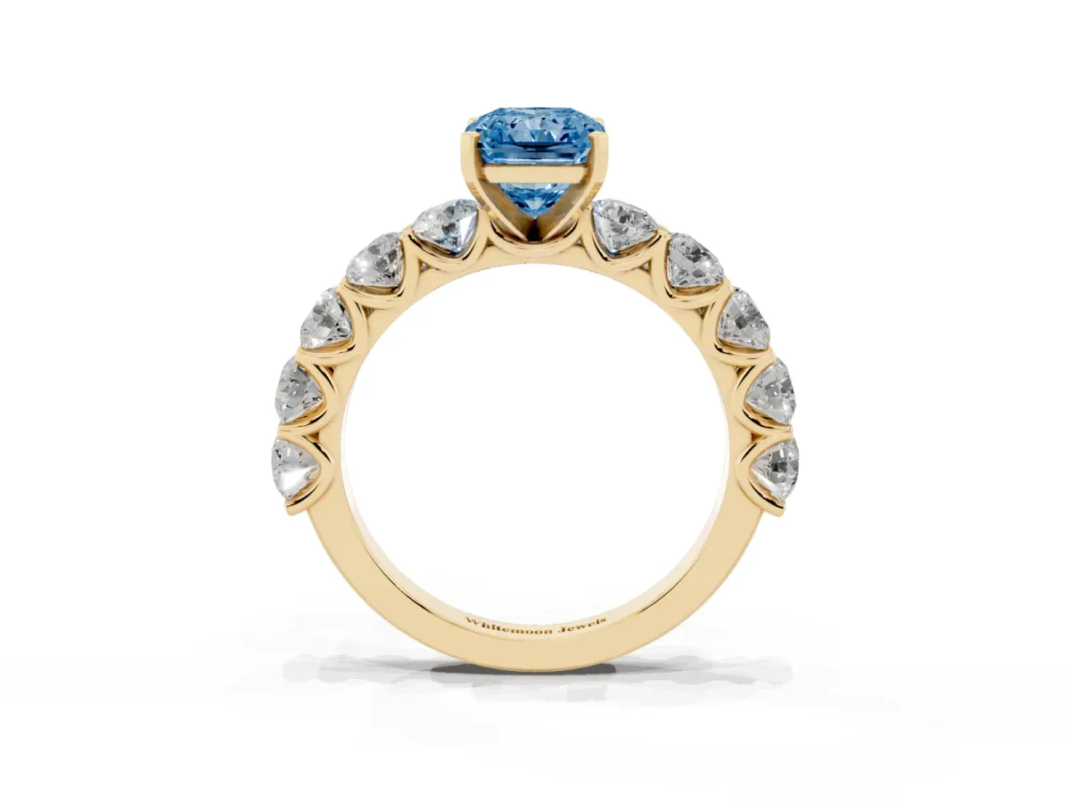 Fancy Blue Radiant Cut Diamond Prong Setting with Side Stones on a Pave Band Yellow gold