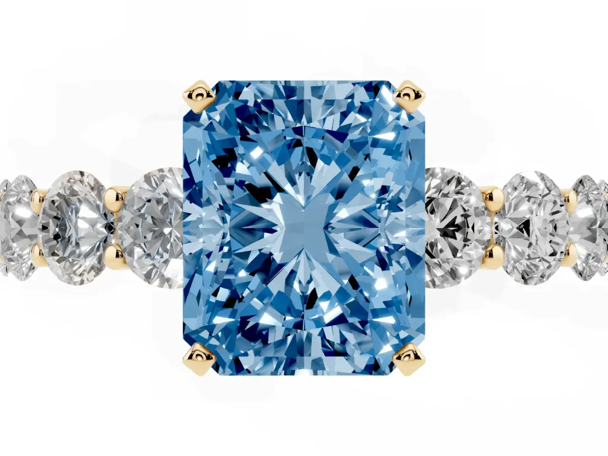 Fancy Blue Radiant Cut Diamond Prong Setting with Side Stones on a Pave Band Yellow gold