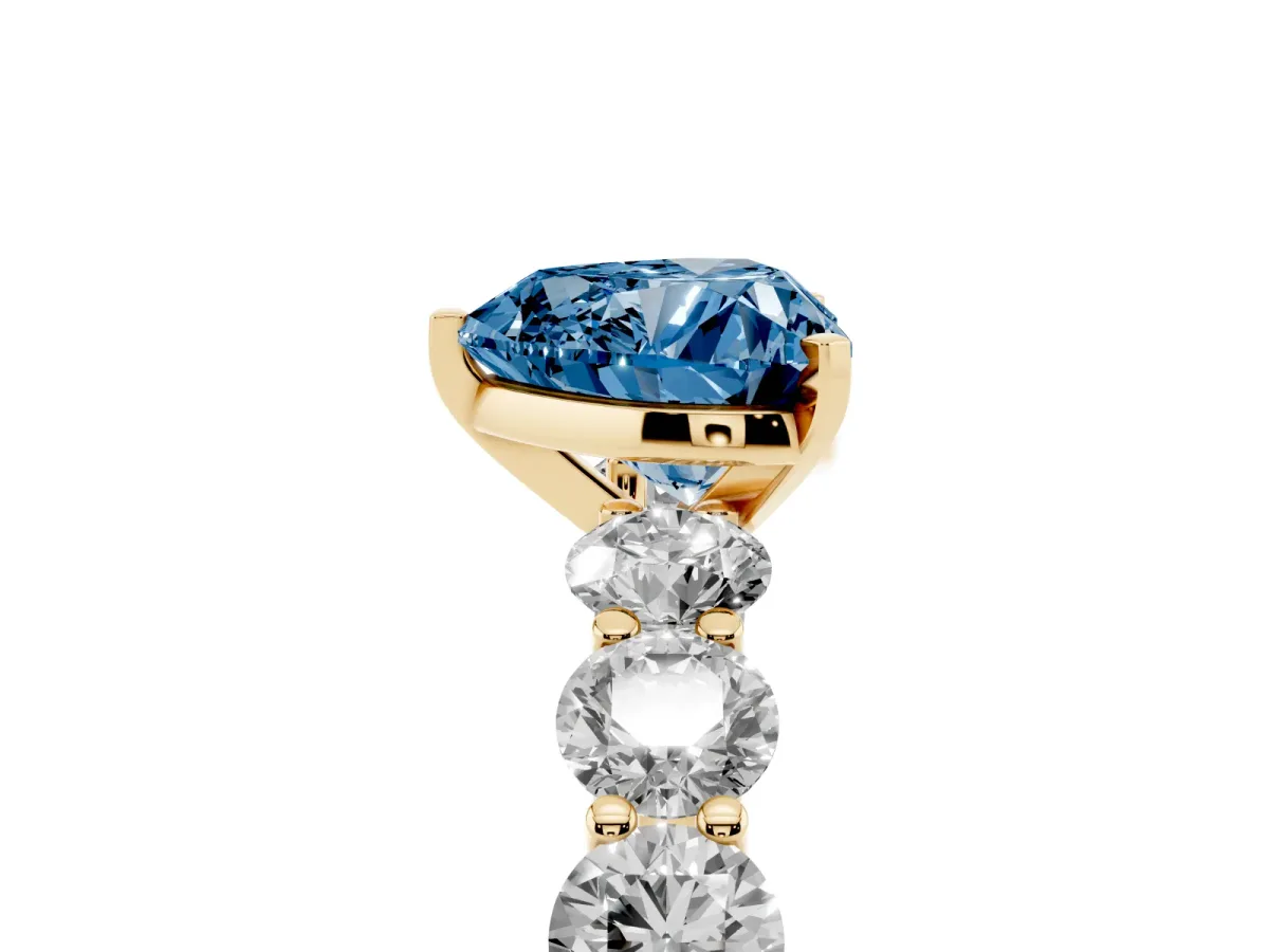 Fancy Blue Heart Cut Diamond Prong Setting with Side Stones on a Pave Band Yellow gold