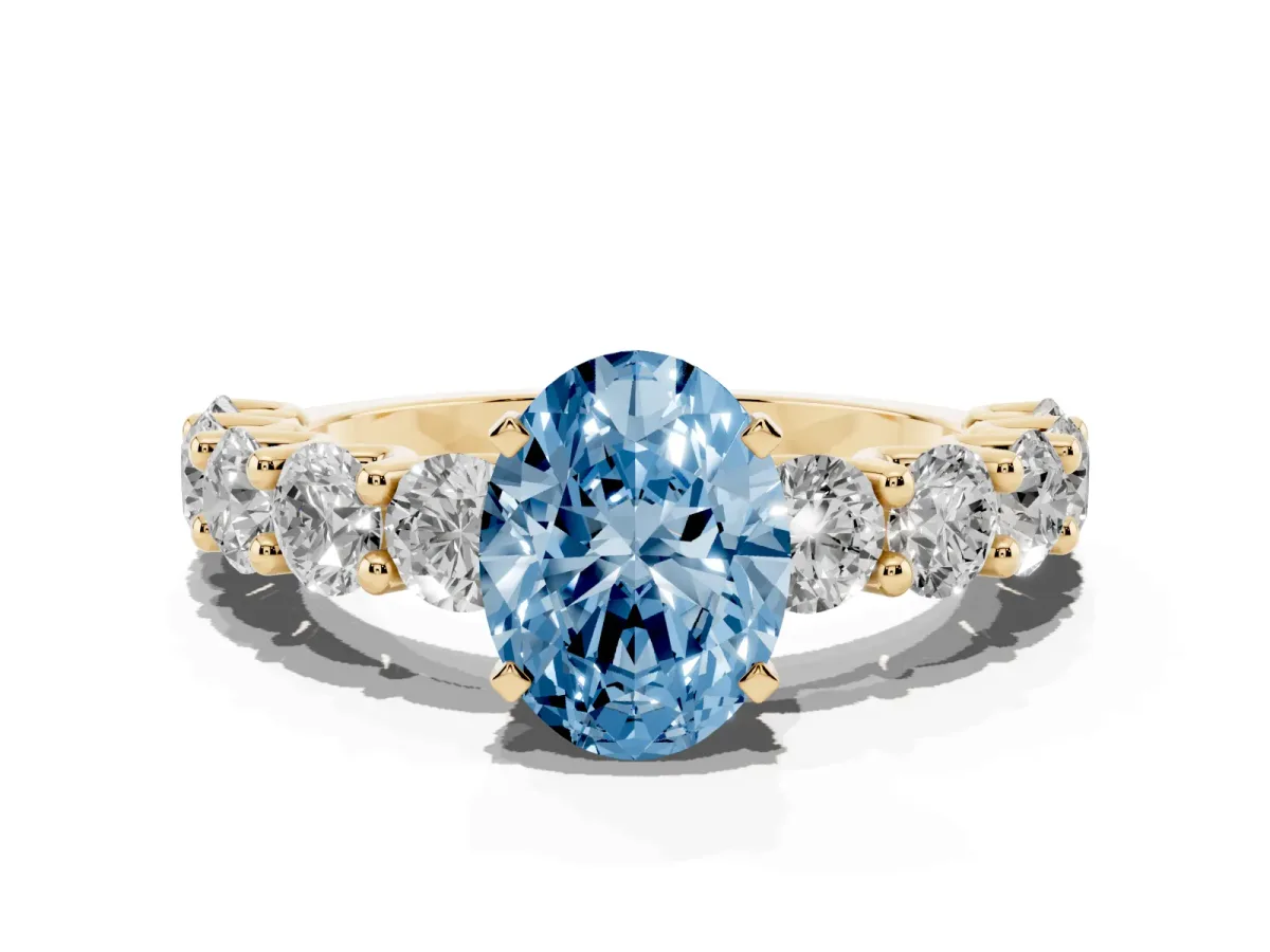 Fancy Blue Oval Cut Diamond Prong Setting with Side Stones on a Pave Band Yellow gold