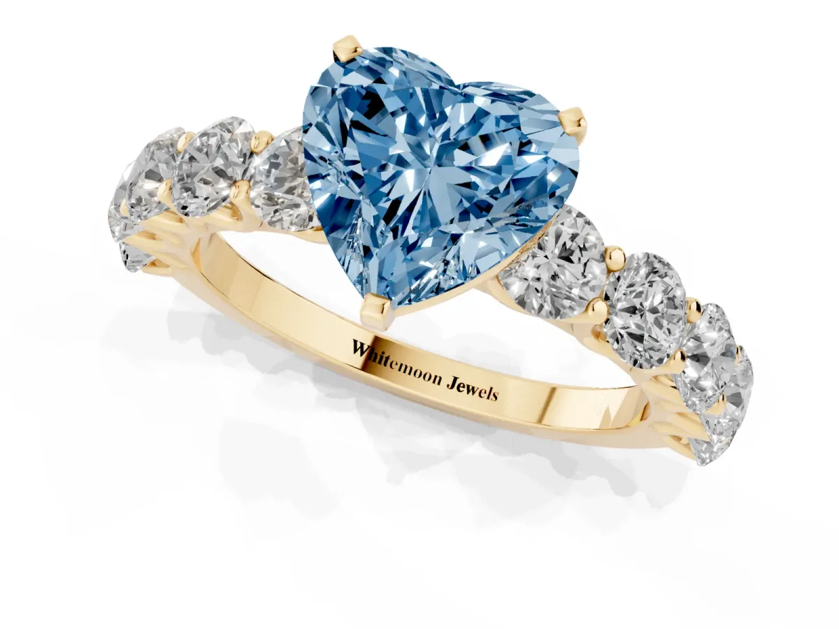 Fancy Blue Heart Cut Diamond Prong Setting with Side Stones on a Pave Band Yellow gold