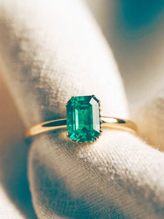 An emerald-cut green emerald ring in yellow gold on linen